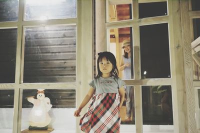 Full length portrait of girl standing against mother standing behind door