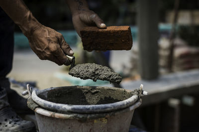 Cropped worker holding cement and brick over container