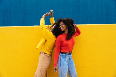 Smiling female friends dancing against wall