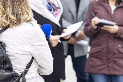 News reporter holding microphone, journalist taking notes during media interview or press conference