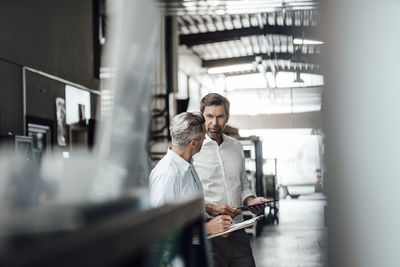 Entrepreneur holding digital tablet while having discussion with colleague at industry