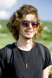 Portrait of young man wearing sunglasses while standing at farm against sky