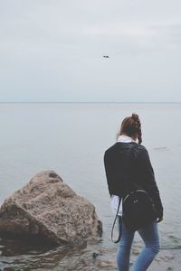 Rear view of woman standing on beach against sky