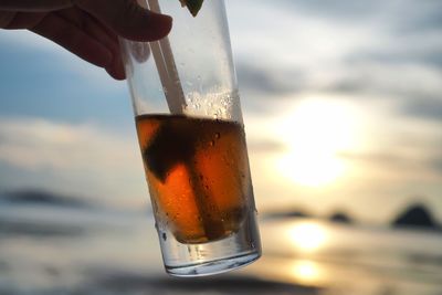 Close-up of hand holding drink against sky during sunset