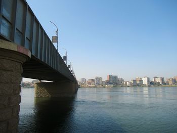 Bridge over river by buildings against clear sky