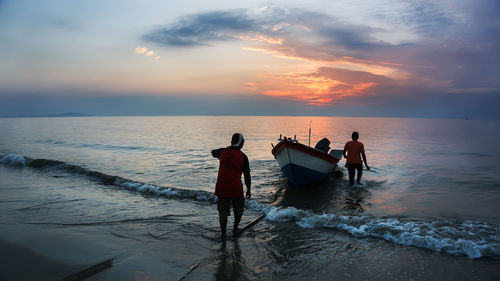 People at beach against sky during sunset