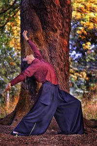 Woman posing standing by tree trunk in forest