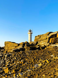 Low angle view of lighthouse by building against clear blue sky