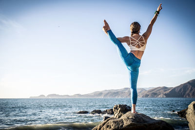 Man standing on rock by sea against sky