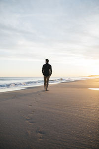 Rear view of man walking on beach against sky