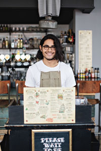 Portrait of smiling owner standing at lectern in restaurant