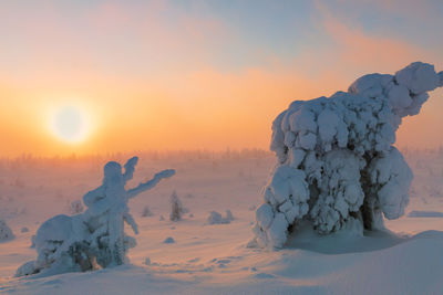 Snow covered landscape against sky during sunset