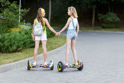 Friends holding hands while standing on segway over footpath