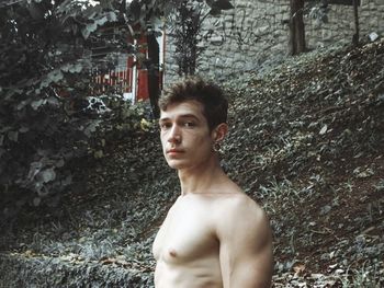 Portrait of shirtless young man standing against trees