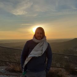 Portrait of man standing by railing against sky during sunset