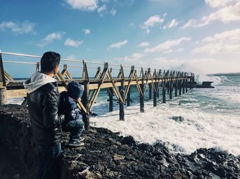 Man with son by retaining wall at beach against sky