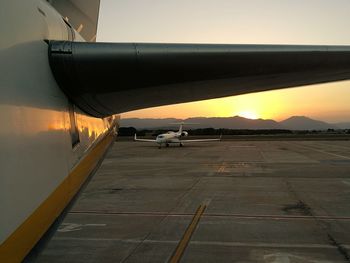 Airplane at airport runway against sky during sunset