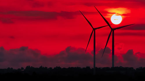 Low angle view of silhouette cranes against orange sky