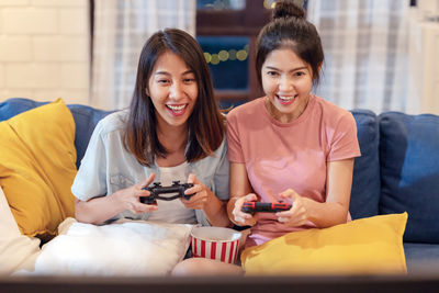 Happy young women playing video game while sitting on sofa at home