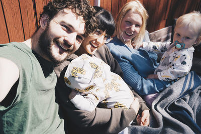 Portrait of cheerful man and women with children sitting at holiday villa on sunny day