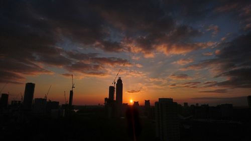 Silhouette of city against cloudy sky during sunset