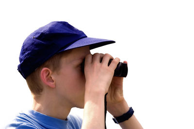 Side view of teenage boy looking through binoculars while standing against clear sky