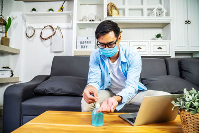 Young man wearing mask using hand sanitizer at home