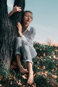 Woman sitting on grass by tree trunk during autumn