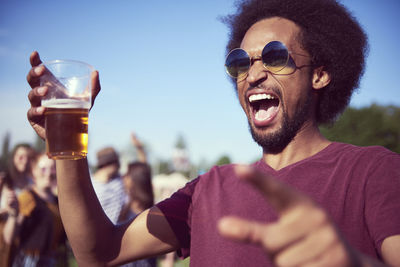 Young man screaming while enjoying beer during sunny day