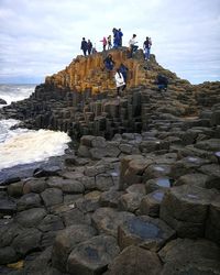 People on rock by sea against sky