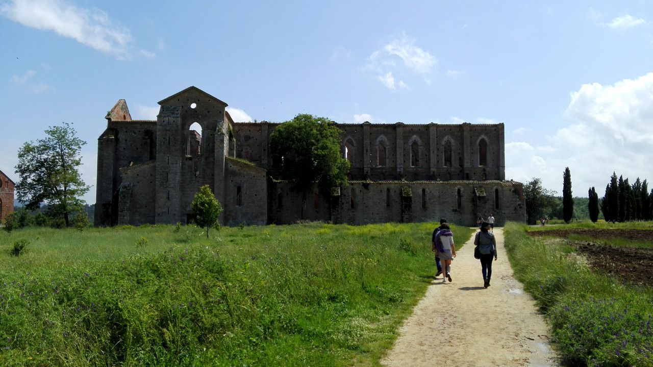 architecture, built structure, rear view, full length, walking, grass, sky, building exterior, men, person, history, old ruin, tourism, tourist, the way forward, outdoors, surface level, day, famous place, the past, culture, footpath, cloud - sky, lawn, castle