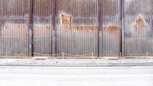 Fence by road against wall during sunny day