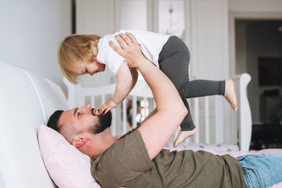 Happy father young man and baby girl little daughter having fun on bed in at home