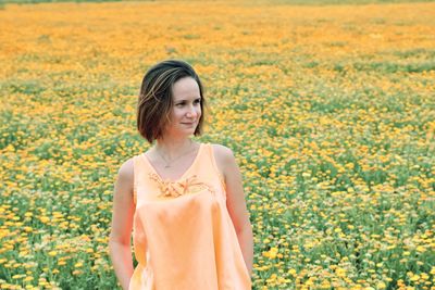 Young woman standing amidst yellow flowering plants on field