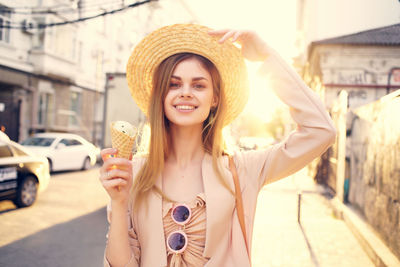 Portrait of young woman holding hat standing in city