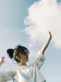 Young woman with arms raised looking away against sky