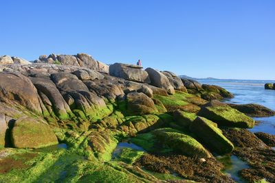 Rock formations by sea against clear blue sky