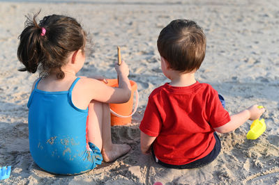 Siblings in bathing suits playing with beach toys in the sand