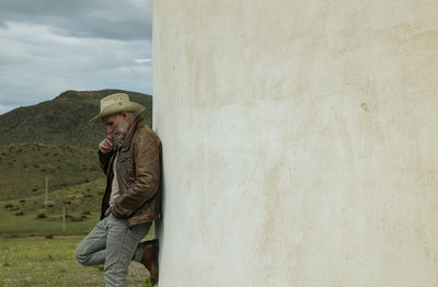 Adult man in cowboy hat standing against white wall in field