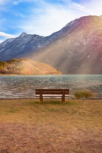Bench by lake against mountains during winter
