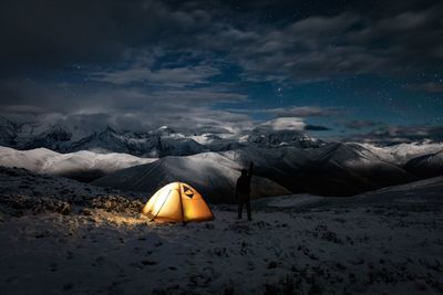 Silhouette man standing by illuminated tent on snow covered field