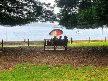 People sitting on bench at beach against sky