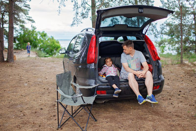 Father and daughter sitting in car trunk