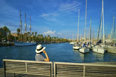 Rear view of woman sitting on pier over lake against sky