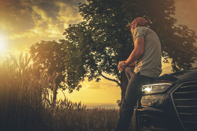 Man standing by tree on field against sky at sunset