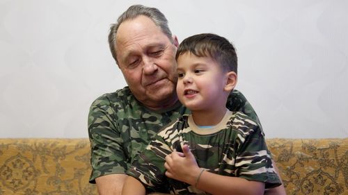 Happy grandfather and grandson sitting on sofa against wall