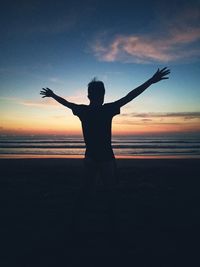 Silhouette boy standing at beach against sky during sunset