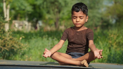 Little boy doing meditate yoga asana with eyes closed outdoor in park.