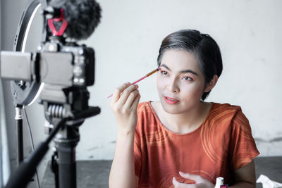 Portrait of young woman holding camera while sitting outdoors