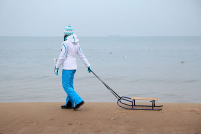 Full length of woman with sledge walking at beach during winter